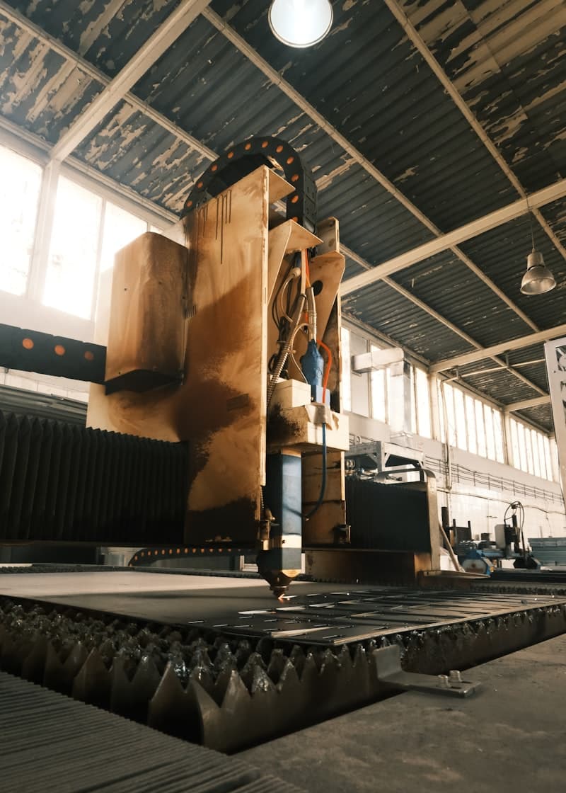 Geniş pencerelerden ışık alan eski bir fabrika salonunda, çelik levha üzerinde çalışan büyük bir CNC kesim makinesi